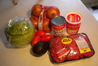 This photo contains all the ingredients needed to complete the Mexican torta recipe including meat, lettuce, tomato, avocado, onions, refried beans, and sour cream.